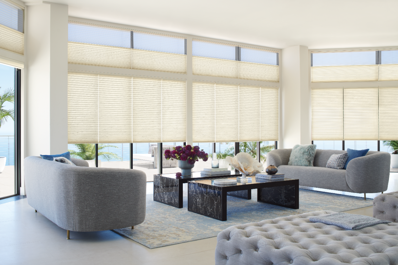 Living room with sofa, accent chairs, and coffee tables set in front of multiple tall windows with Duette Honeycomb shades.
